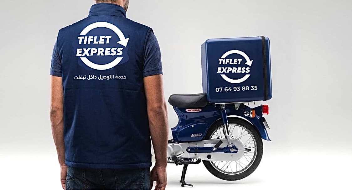 عامل توصيل يرتدي سترة زرقاء يقف بجانب دراجة نارية زرقاء تحمل شعار تيفلت إكسبريس.